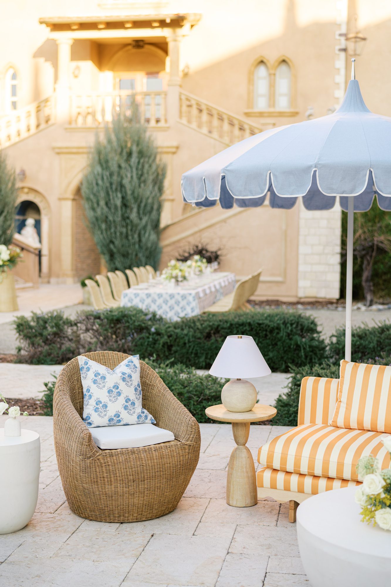 Outdoor lounge seating with woven chair, striped upholstery, and coastal color palette in an Italian courtyard setting.
