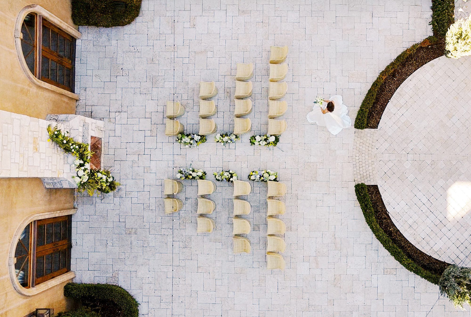 Overhead view of outdoor wedding ceremony with woven chairs arranged in rows in an Italian-inspired courtyard.