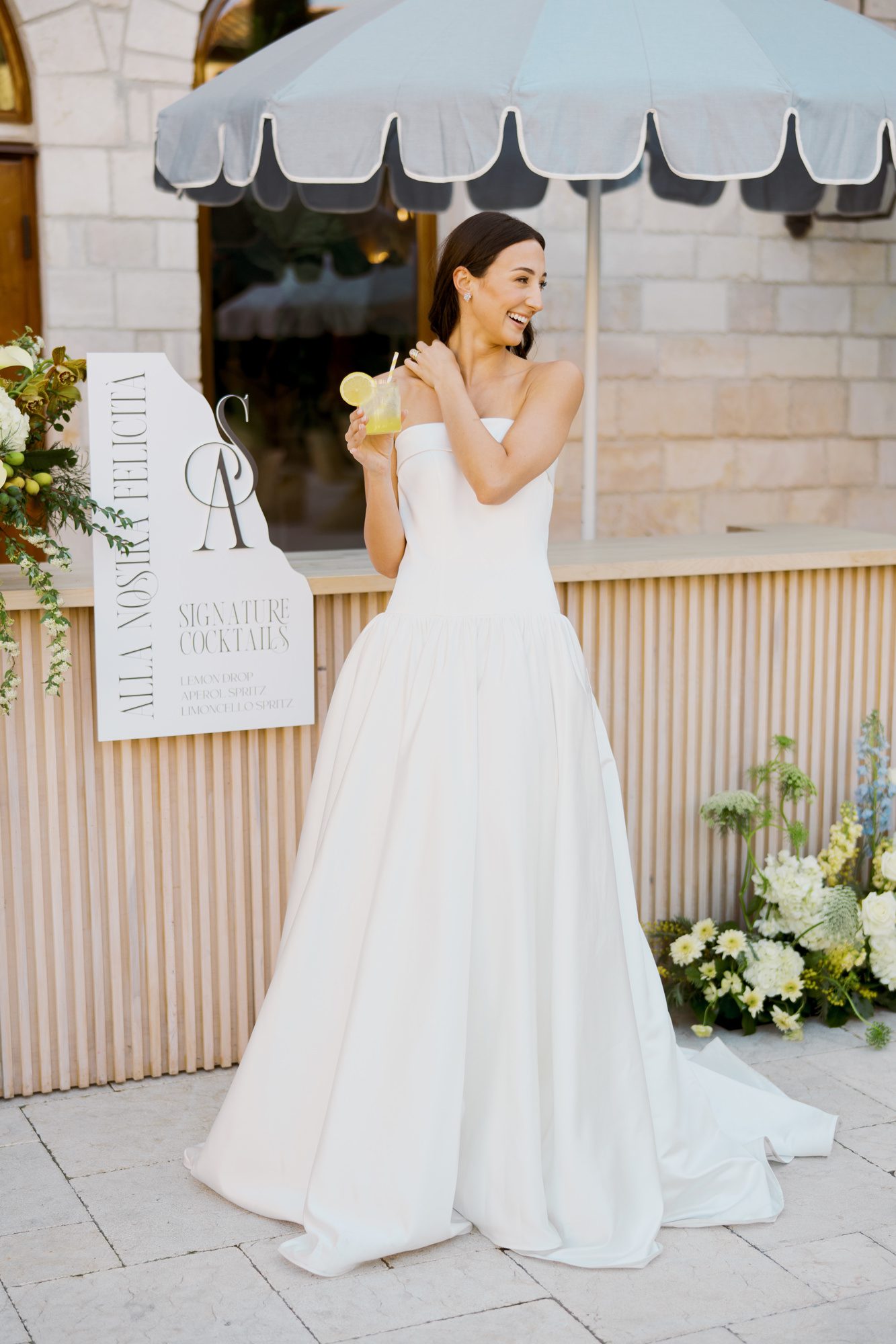 Bride standing beside custom wedding signage featuring modern typography and curved silhouette.