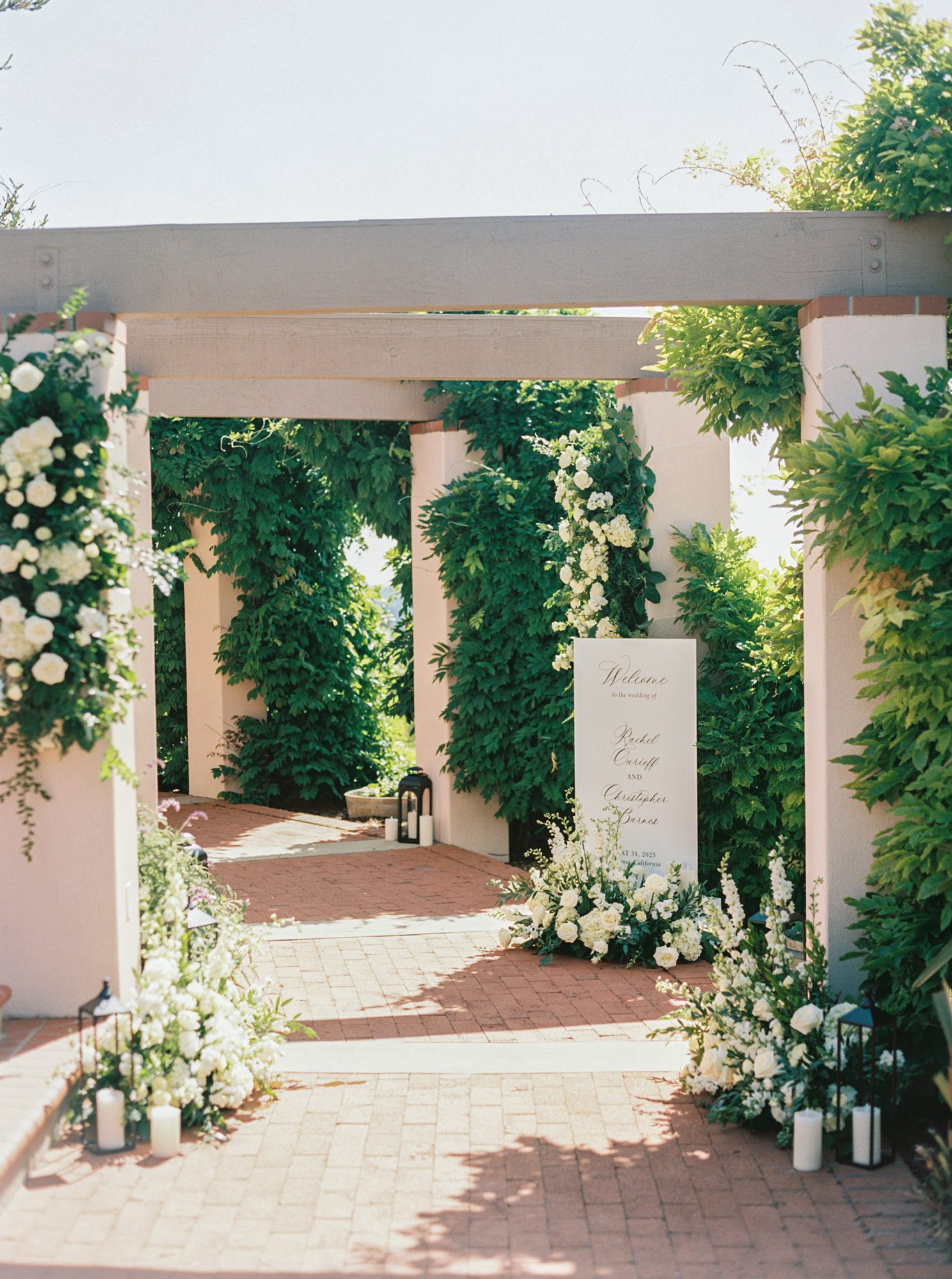 Outdoor wedding ceremony aisle with white florals and greenery arch in garden setting