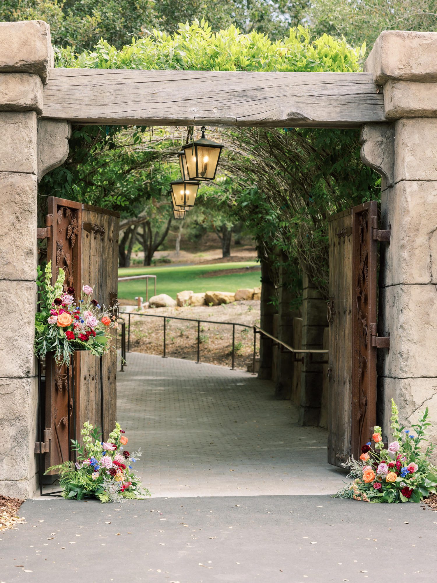 Garden ceremony entrance with wooden gates, lanterns, and colorful floral arrangements