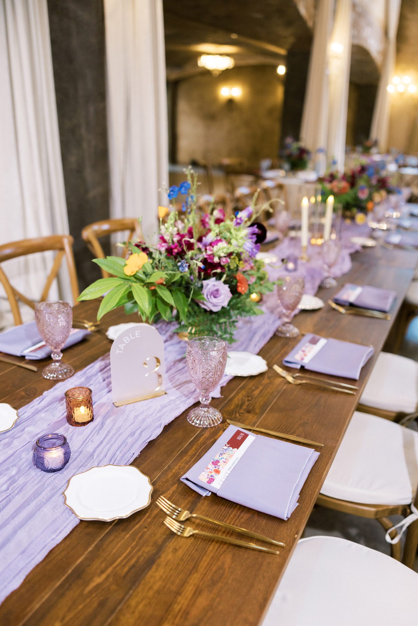 Reception table with lavender runner, colorful florals, and layered place settings
