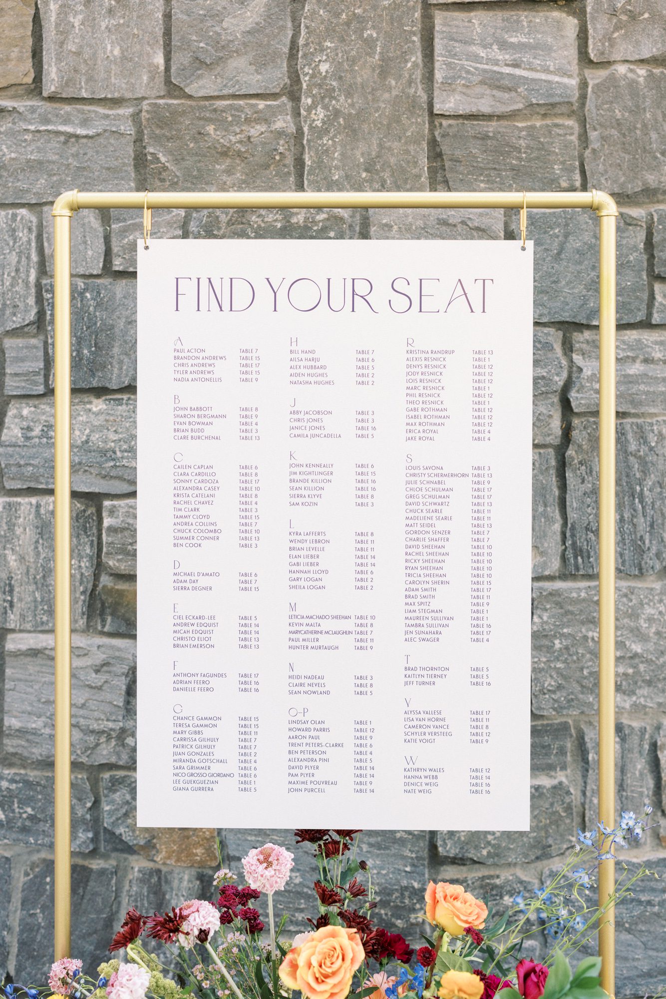 Minimalist wedding seating chart displayed on fabric panel with floral base
