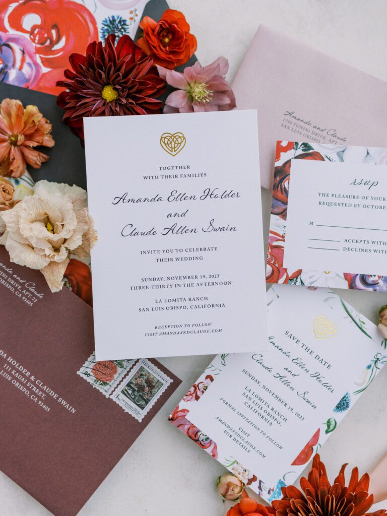 Full invitation suite displayed with watercolor details, blush envelopes, floral accents, and textured stamps.