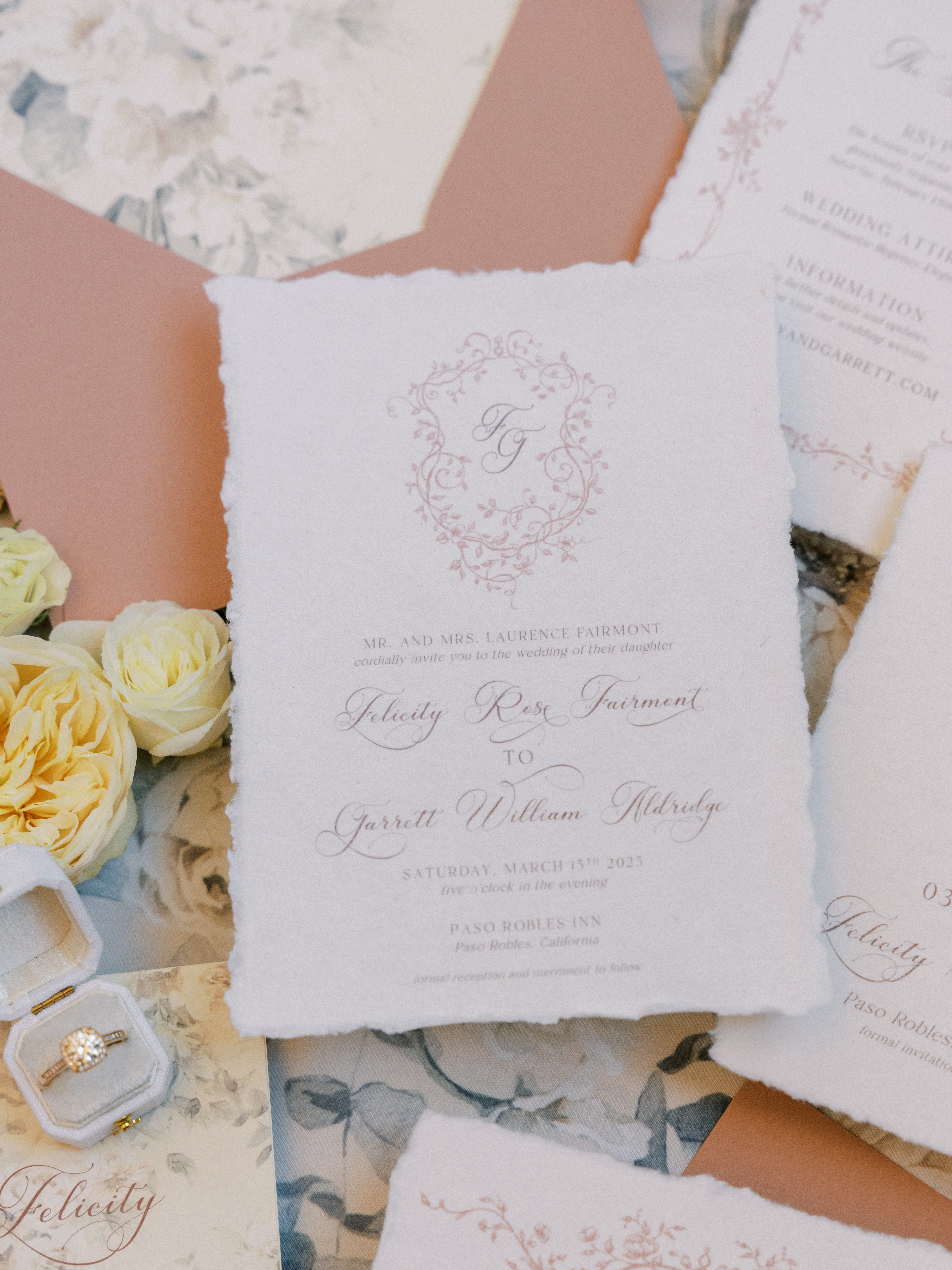 Hand-torn wedding invitation with monogram crest styled with blush ribbon and roses for a San Luis Obispo wedding