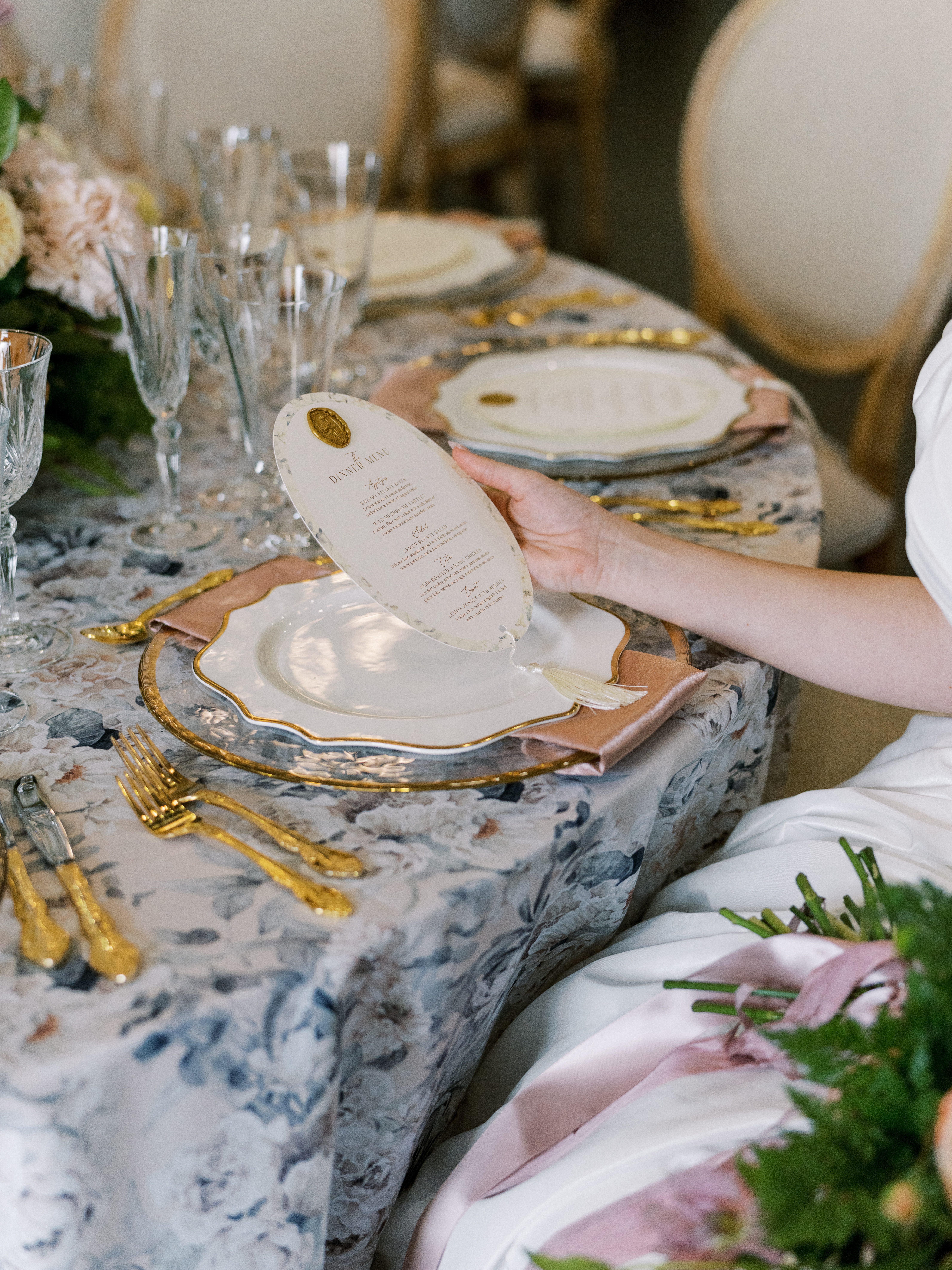 Oval wedding dinner menu placed on layered china with gold flatware and blush napkin