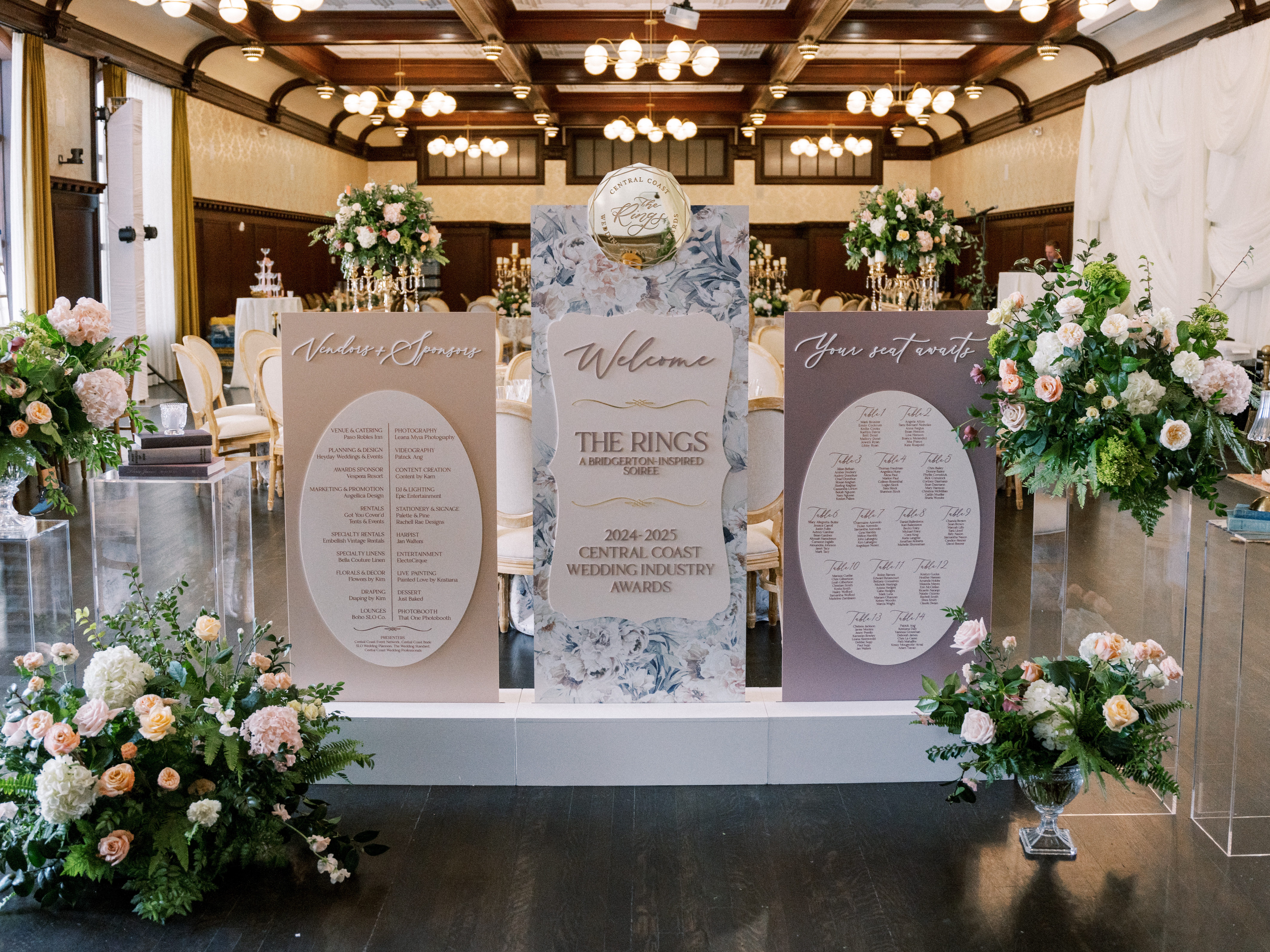 Regency-inspired welcome signage and seating chart styled with florals in a historic San Luis Obispo ballroom