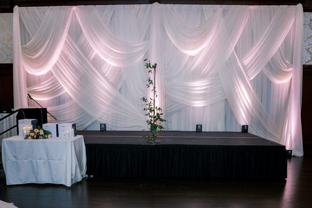 Draped stage backdrop with soft blush lighting and greenery for wedding awards ceremony