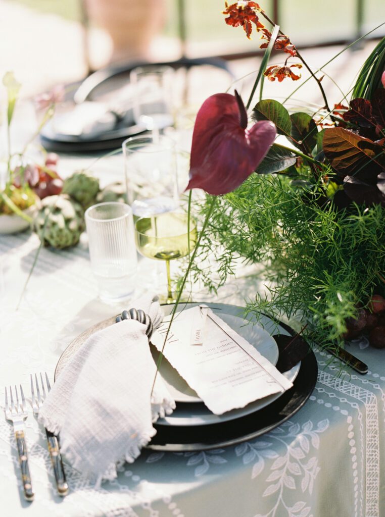 Modern wedding tablescape with layered place setting, handmade paper menu, green glassware, and organic florals