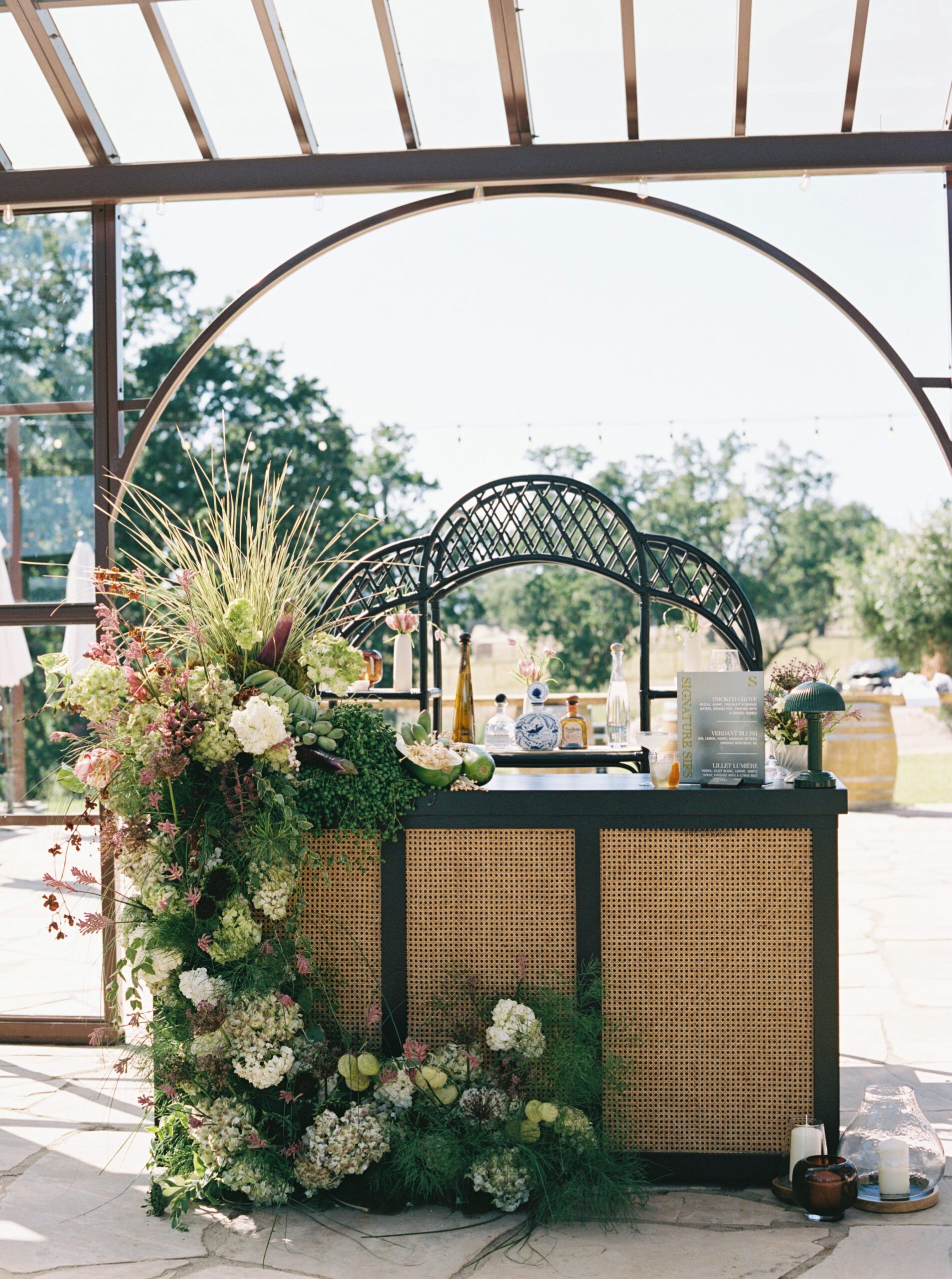 Green wedding bar with custom signature cocktail signage and organic floral installation at Riata Ranch.