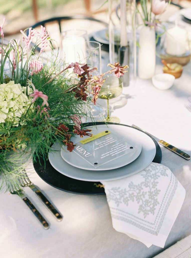 Custom frosted acrylic wedding menu layered over a modern place setting with botanical florals
