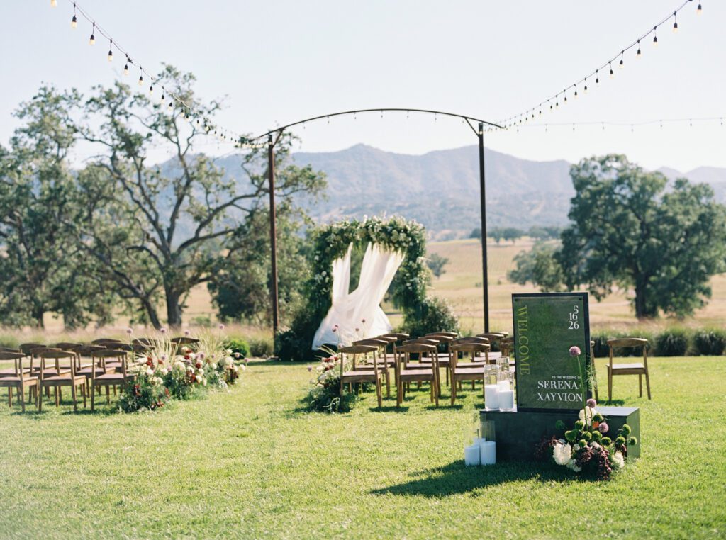 Outdoor Riata Ranch wedding ceremony with custom welcome sign, floral aisle arrangements, and mountain views
