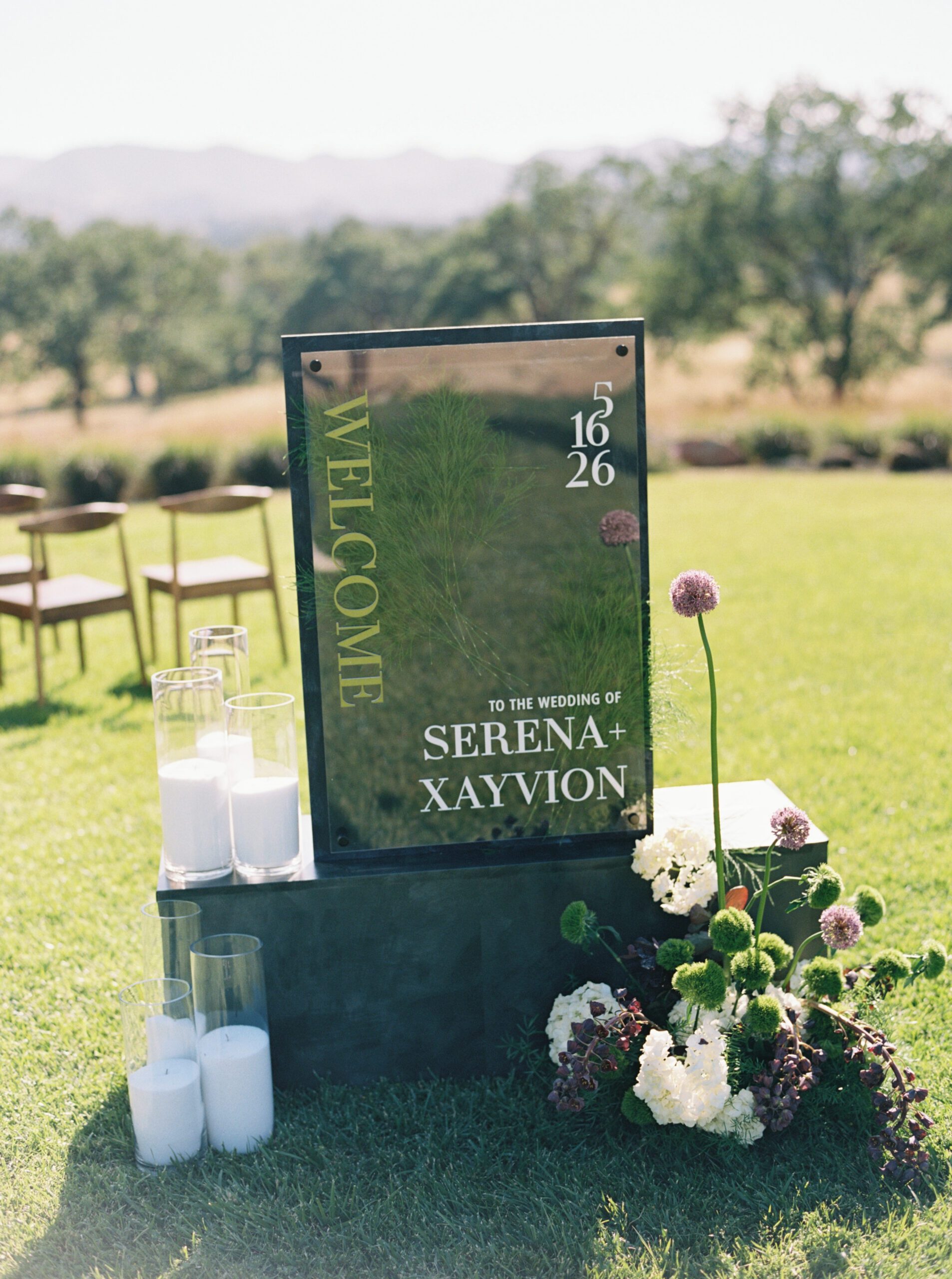 Custom acrylic wedding welcome sign for Serena and Xayvion surrounded by candles and organic florals at Riata Ranch