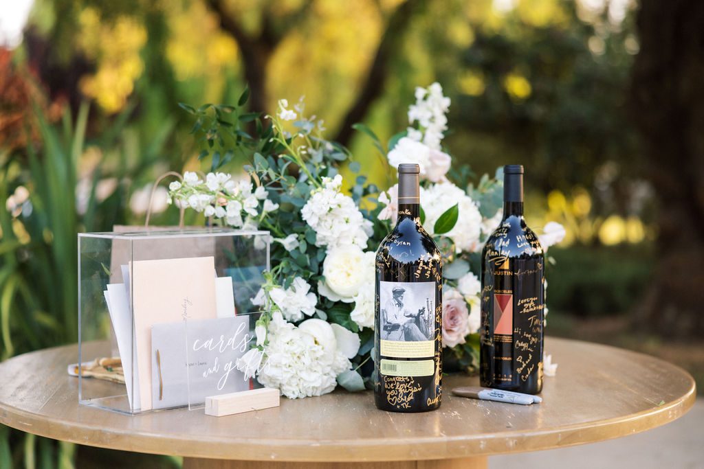 Wedding cards and gifts table with floral arrangement and signed wine bottles